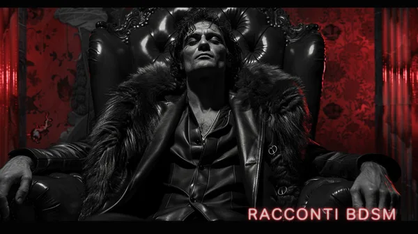 Ritratto in bianco e nero di un uomo seduto su poltrona di pelle con giacca di pelliccia davanti a parete rossa.